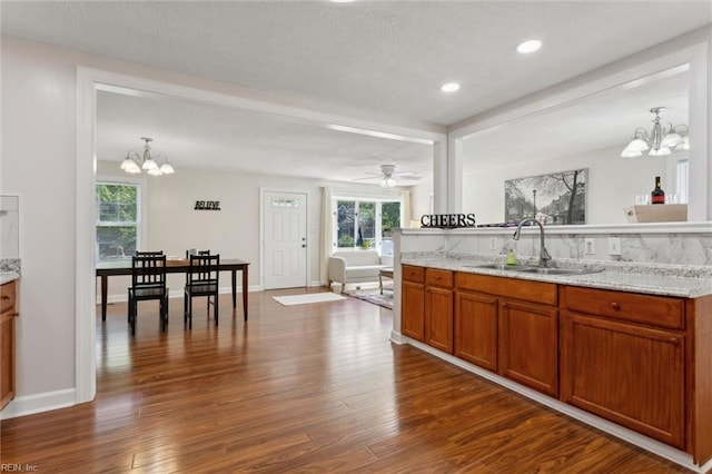 kitchen featuring dark wood-style floors, a sink, light stone counters, and brown cabinetry