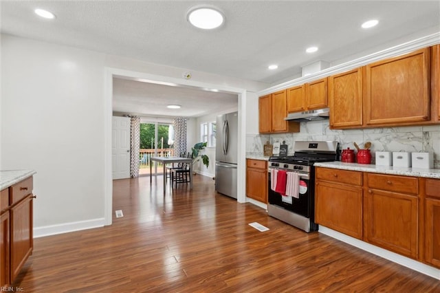 kitchen with under cabinet range hood, baseboards, appliances with stainless steel finishes, and dark wood-style floors