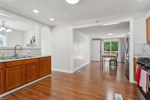 kitchen with brown cabinets, a sink, appliances with stainless steel finishes, dark wood-type flooring, and backsplash