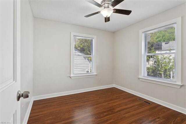empty room featuring baseboards, visible vents, dark wood-style flooring, and plenty of natural light