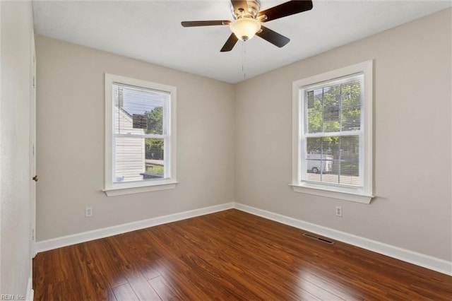 spare room with dark wood-style floors, baseboards, visible vents, and a ceiling fan