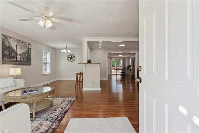 living room with baseboards, wood finished floors, and ceiling fan with notable chandelier