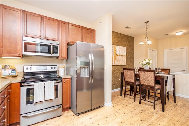 kitchen featuring brown cabinets, light wood-style flooring, appliances with stainless steel finishes, a chandelier, and visible vents