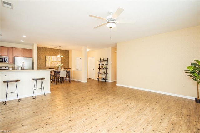 living room featuring ceiling fan with notable chandelier, visible vents, baseboards, and light wood-style floors
