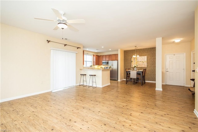 living room featuring ceiling fan with notable chandelier, baseboards, and light wood-style floors
