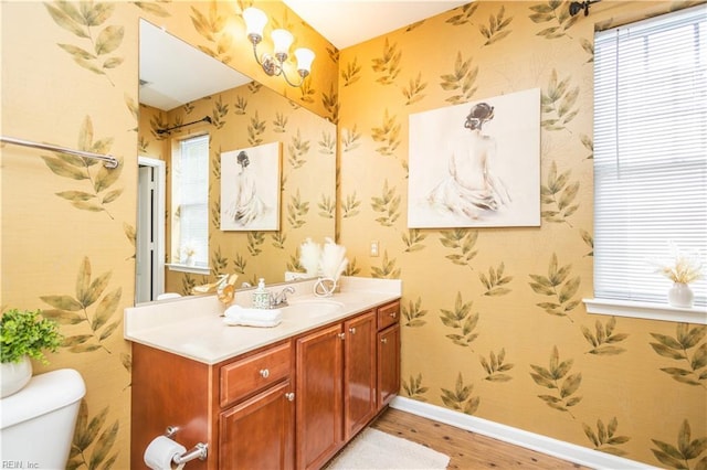 bathroom featuring vanity, toilet, baseboards, wallpapered walls, and wood finished floors