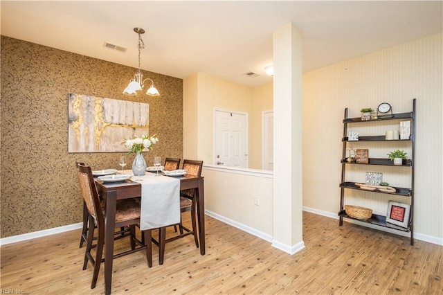 dining space featuring visible vents, wood finished floors, a notable chandelier, and wallpapered walls