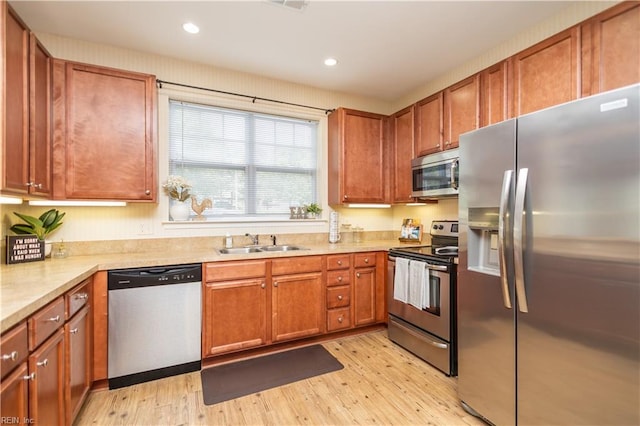 kitchen with light wood-type flooring, stainless steel appliances, light countertops, and a sink