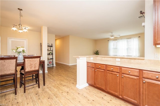 kitchen with pendant lighting, light wood-style flooring, light countertops, a peninsula, and brown cabinetry
