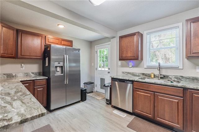 kitchen with light stone counters, a sink, light wood-style floors, stainless steel appliances, and visible vents