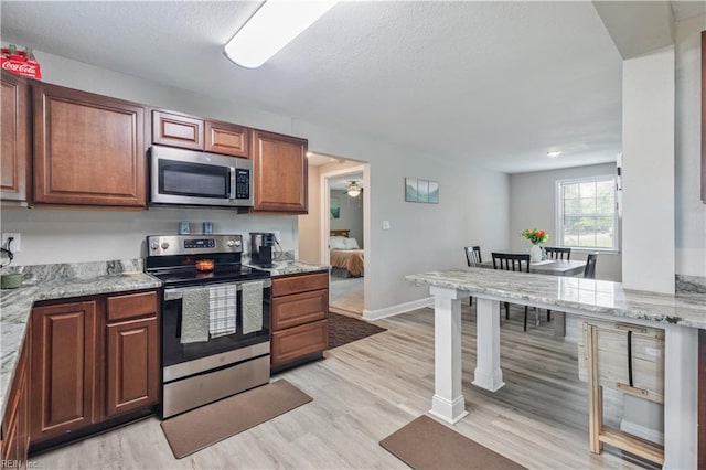 kitchen with light stone counters, light wood-style flooring, baseboards, and stainless steel appliances
