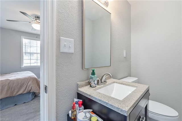 bathroom featuring vanity, a textured wall, a ceiling fan, and toilet
