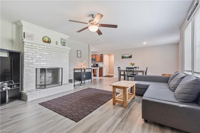 living room with ceiling fan, a brick fireplace, light wood-type flooring, baseboards, and recessed lighting