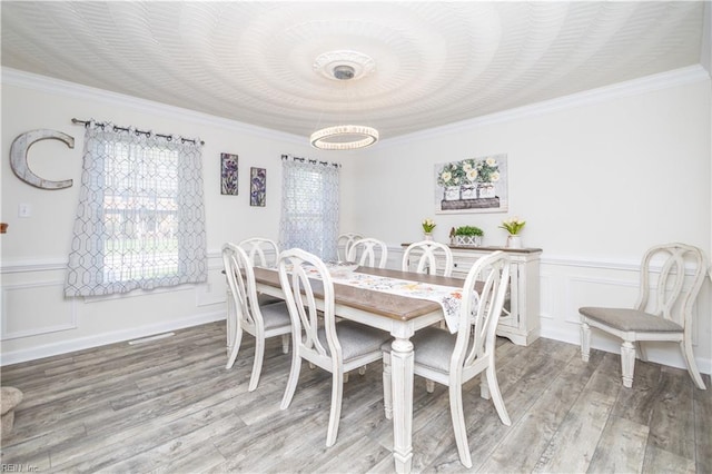 dining room featuring wainscoting, an inviting chandelier, ornamental molding, a decorative wall, and light wood-style flooring