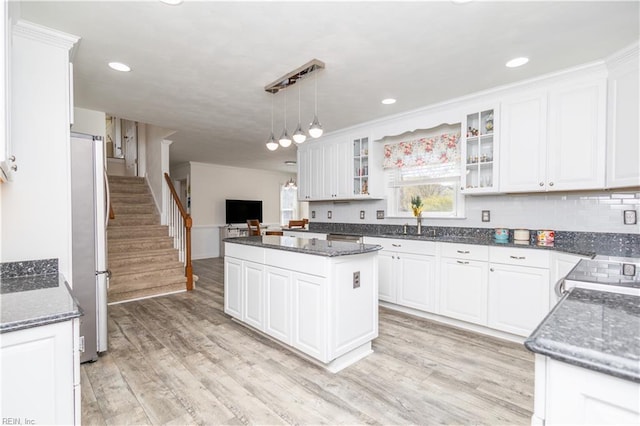 kitchen featuring freestanding refrigerator, white cabinetry, decorative light fixtures, and glass insert cabinets
