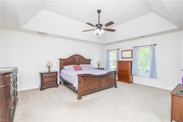bedroom with a tray ceiling, visible vents, light carpet, and baseboards