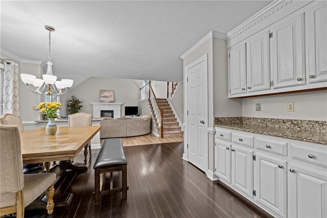 dining room featuring stairway, a glass covered fireplace, an inviting chandelier, ornamental molding, and dark wood-type flooring
