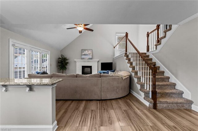 living area with a fireplace, baseboards, ceiling fan, stairway, and light wood-style flooring