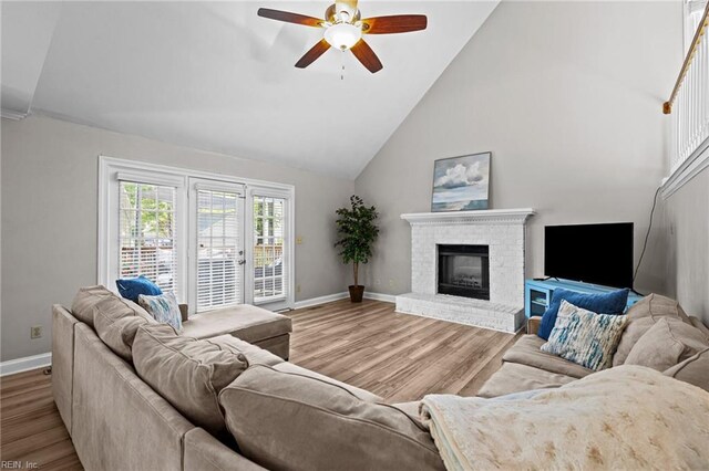 living area featuring a ceiling fan, a brick fireplace, wood finished floors, baseboards, and high vaulted ceiling