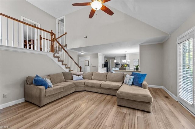 living area with light wood-style floors, high vaulted ceiling, ceiling fan with notable chandelier, baseboards, and stairway