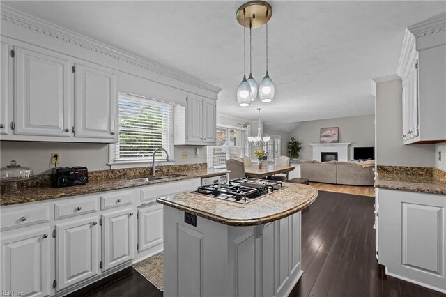 kitchen with a kitchen island, a sink, open floor plan, stainless steel gas stovetop, and white cabinetry