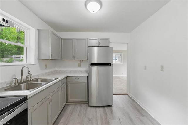 kitchen featuring gray cabinets, freestanding refrigerator, a wealth of natural light, light wood finished floors, and a sink