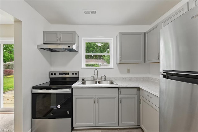 kitchen with appliances with stainless steel finishes, a sink, under cabinet range hood, and gray cabinets