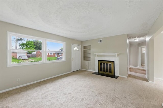 unfurnished living room featuring a brick fireplace, built in shelves, visible vents, carpet, and baseboards