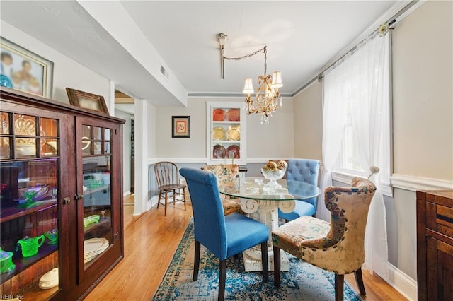 dining space with an inviting chandelier, a wainscoted wall, visible vents, light wood-style flooring, and french doors