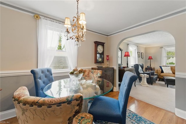 dining room featuring ornamental molding, light wood finished floors, arched walkways, and a notable chandelier