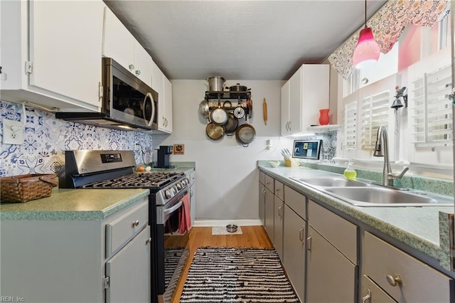 kitchen with light wood-style flooring, a sink, stainless steel appliances, gray cabinets, and backsplash
