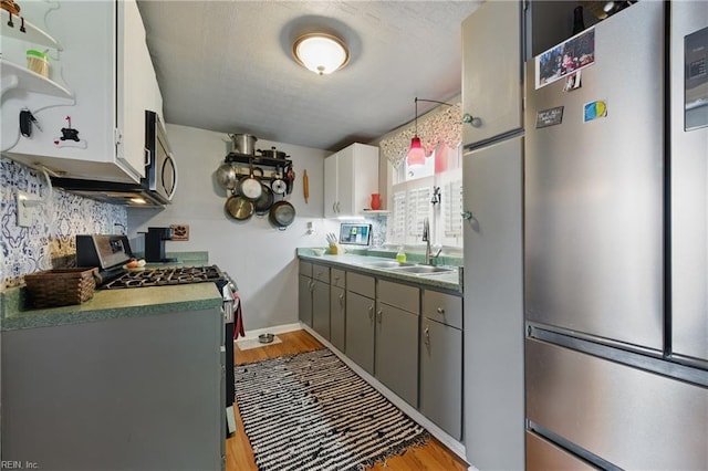 kitchen with gray cabinetry, light wood-style flooring, open shelves, and appliances with stainless steel finishes