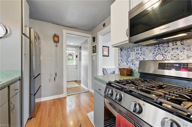 kitchen featuring stainless steel appliances, light wood-style floors, light countertops, baseboards, and visible vents