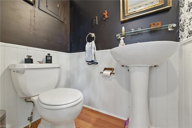 bathroom featuring wood finished floors, toilet, and a wainscoted wall