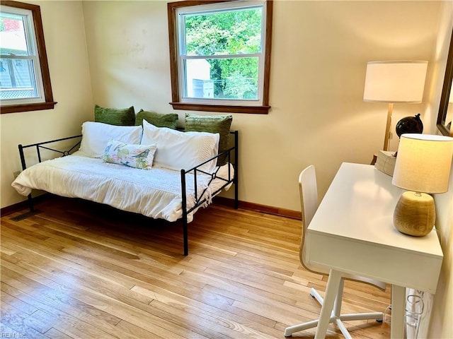 bedroom with multiple windows, light wood-type flooring, and baseboards