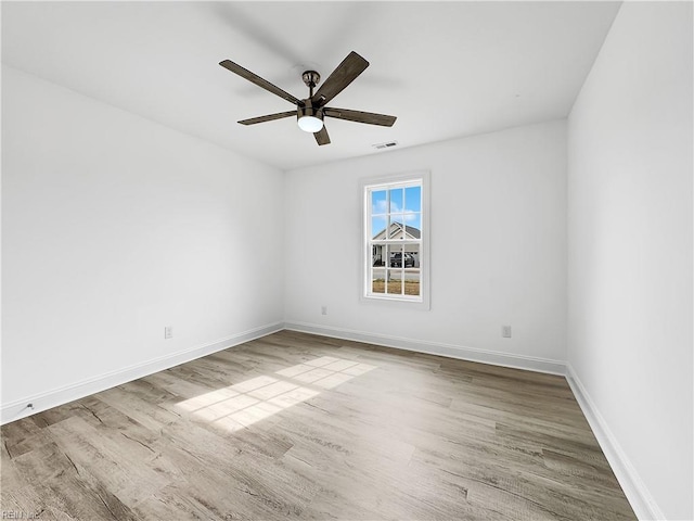 unfurnished room with a ceiling fan, visible vents, wood finished floors, and baseboards