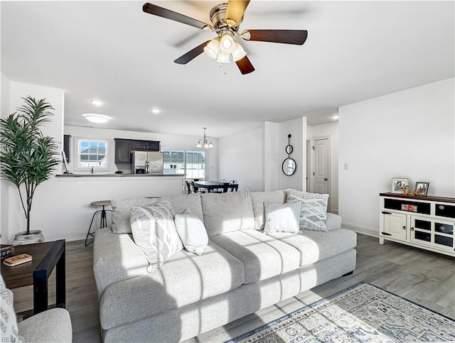 living area featuring wood finished floors, ceiling fan with notable chandelier, and baseboards