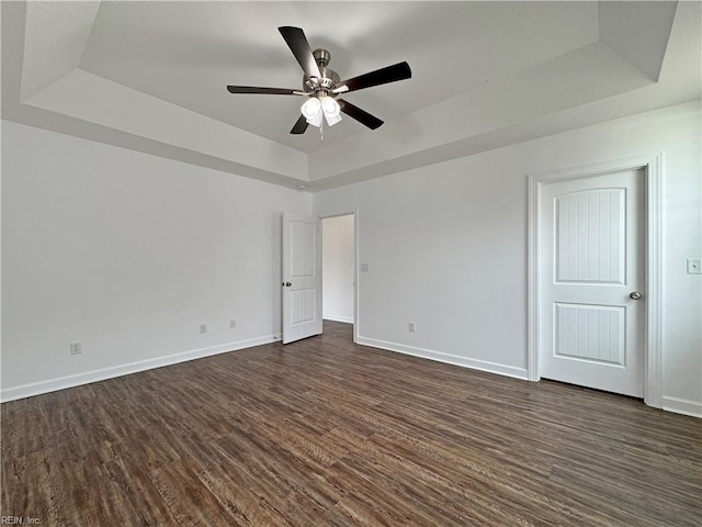 empty room featuring a raised ceiling, a ceiling fan, dark wood-style floors, and baseboards