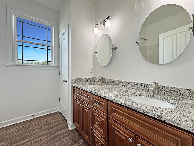 full bath with baseboards, wood finished floors, double vanity, and a sink