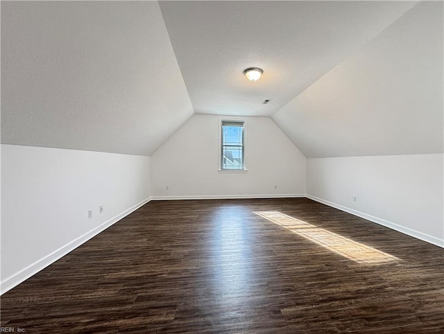 bonus room with dark wood finished floors, vaulted ceiling, and baseboards