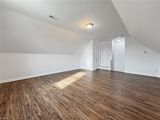 bonus room featuring dark wood-type flooring, visible vents, vaulted ceiling, baseboards, and a textured ceiling