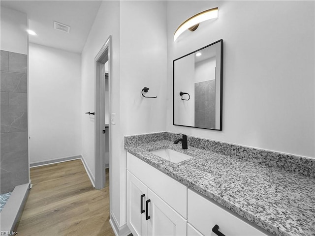 bathroom featuring a tile shower, vanity, visible vents, and wood finished floors