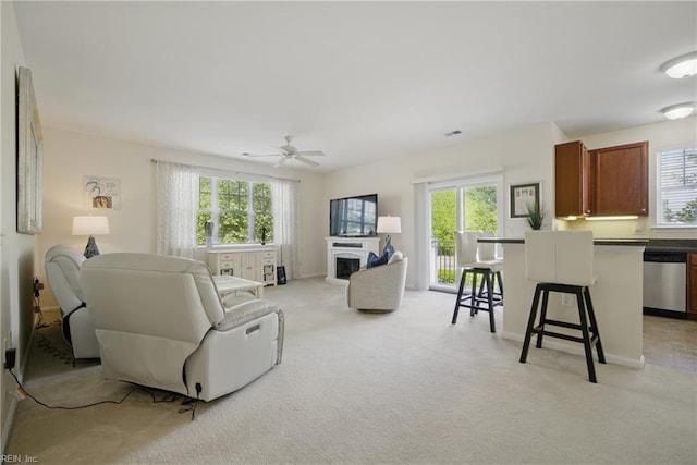 living area featuring ceiling fan, light colored carpet, and a healthy amount of sunlight