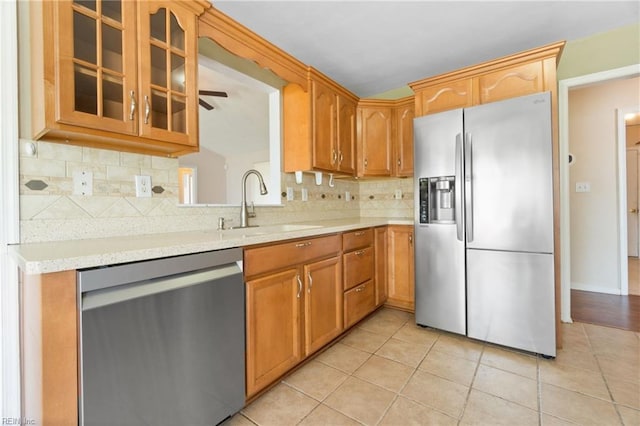 kitchen featuring tasteful backsplash, glass insert cabinets, light tile patterned floors, appliances with stainless steel finishes, and light countertops