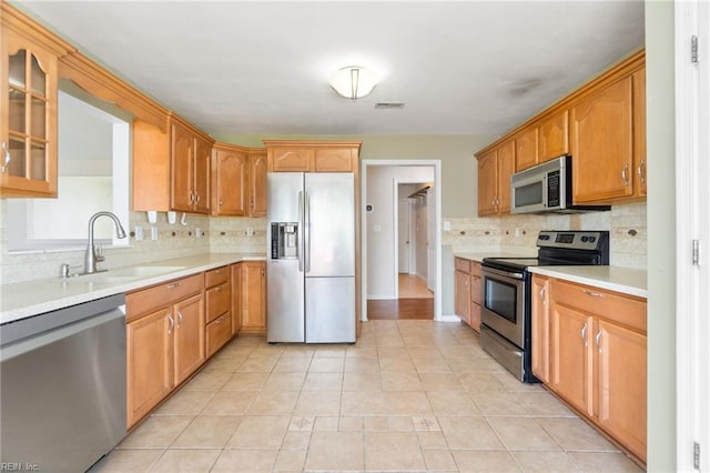 kitchen with a sink, stainless steel appliances, decorative backsplash, glass insert cabinets, and light countertops