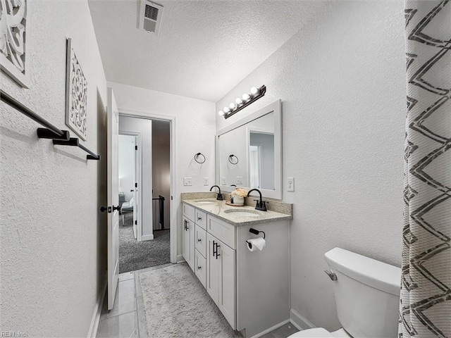 bathroom with visible vents, double vanity, a textured wall, and a sink