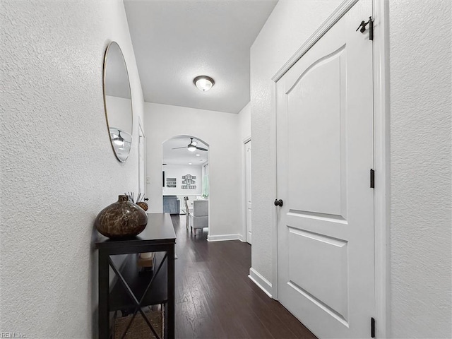corridor featuring baseboards, dark wood-style flooring, and a textured wall