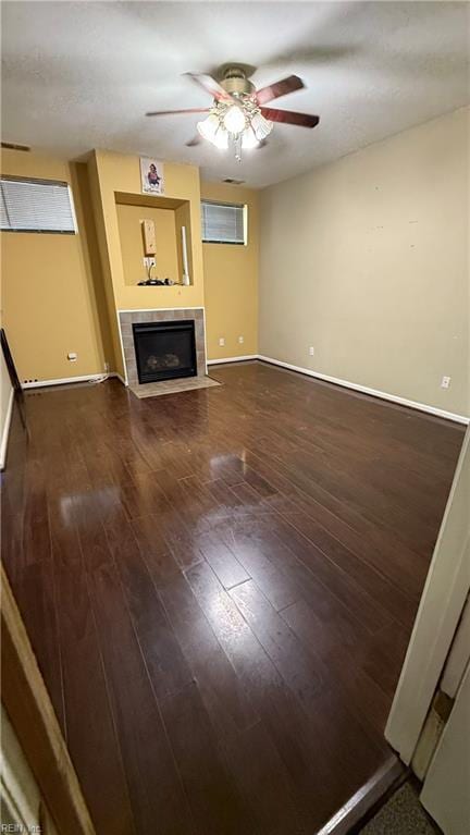 unfurnished living room with baseboards, wood finished floors, a ceiling fan, and a tile fireplace