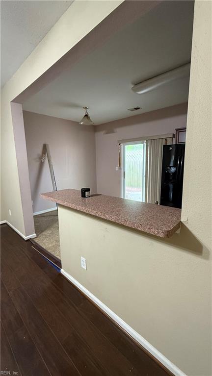 interior space with dark wood-style flooring, black fridge, and baseboards