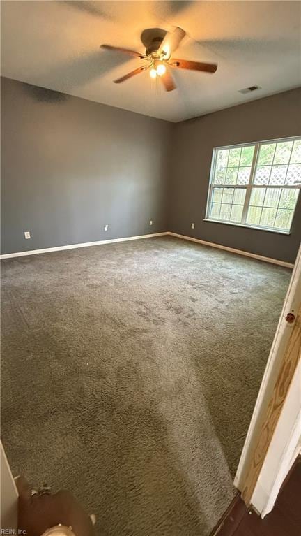 empty room featuring ceiling fan, baseboards, dark colored carpet, and visible vents